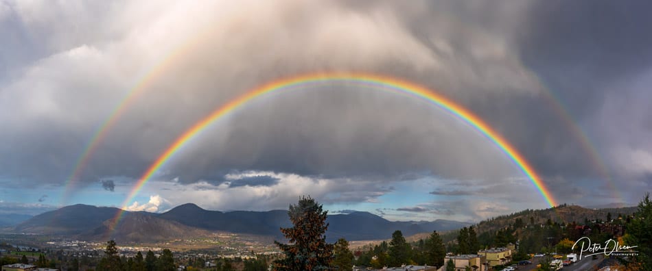 Kamloops City double rainbow with fluffy clouds and blue sky with tree tops