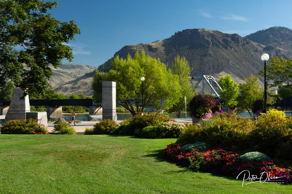 Kamloops City park with clean-cut lawn and bushes with flowers and trees with mountain