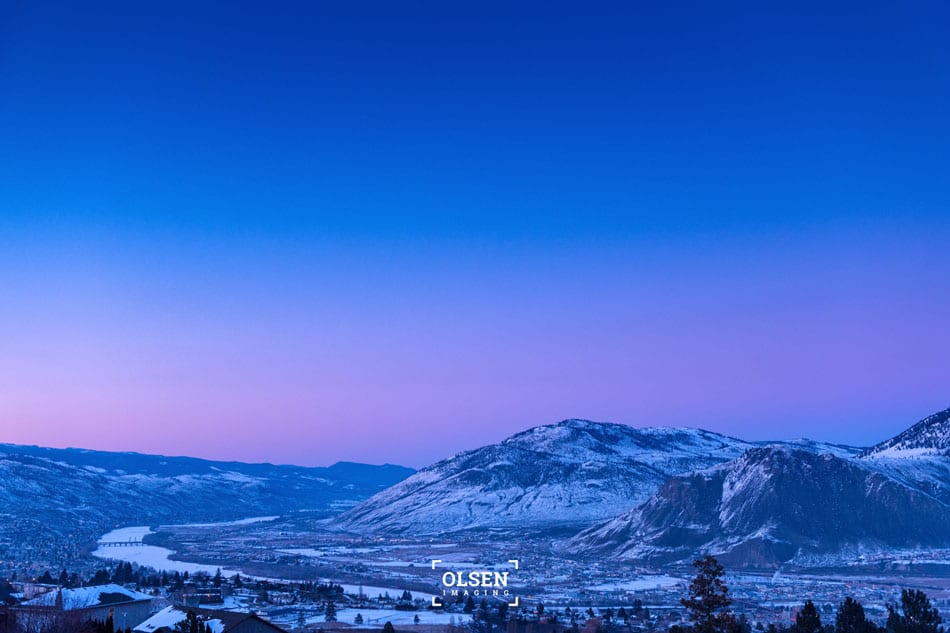 Blue and pink sky over snowy mountain with city and river