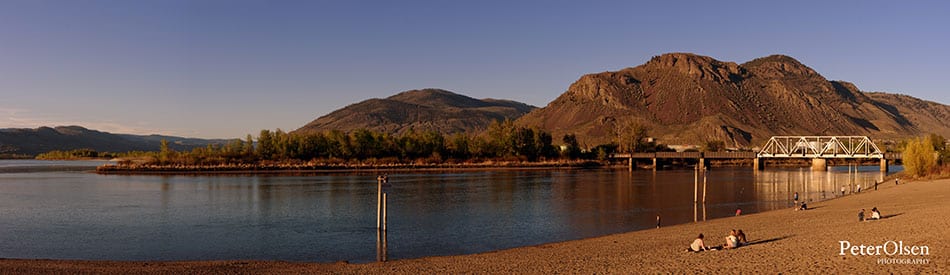 Kamloops City people on a beach near the river with a white bridge