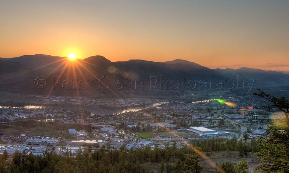 Photograph of a city near mountains and sun riding behind it