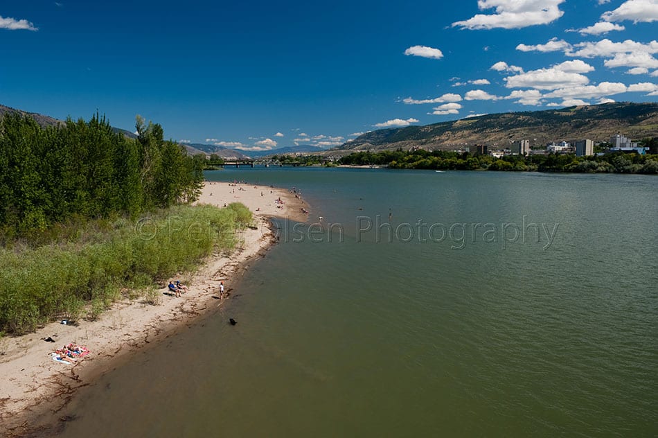 Kamloops City green grass with shoreline and mountain with white clouds and long river
