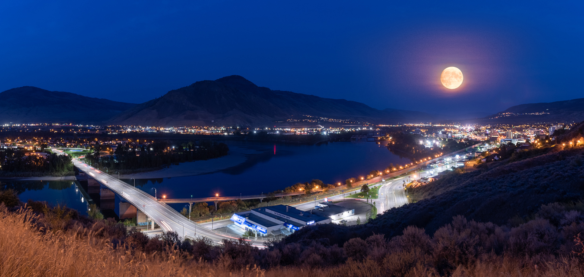 panoramic HDR view of the city at night with mountains and lake with cars