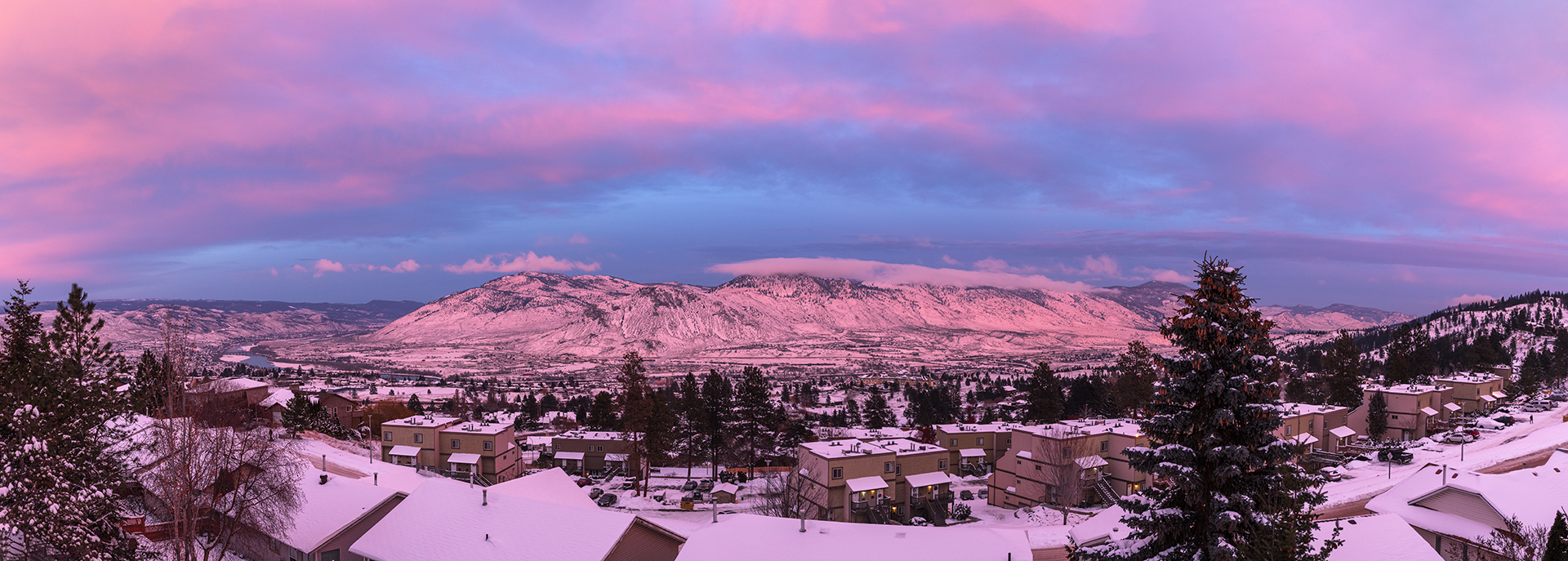 snowy city with trees and mountain with blue and pink clouds