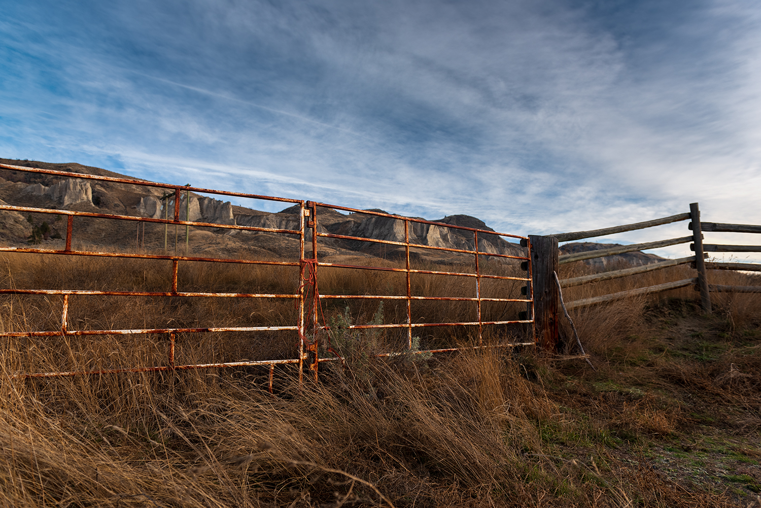Kamloops rural life rusted fence against tall grass and mountain with blue sky and clouds