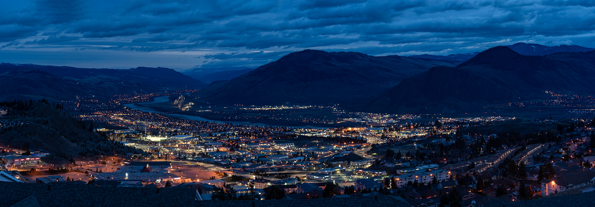 panoramic view of a city with lights and clouds and mountains
