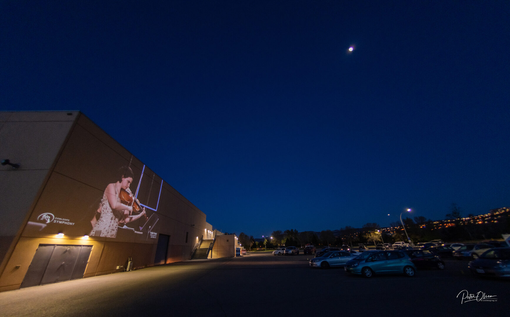 blue sky and full moon with lights in a carpark with a violinist on a building