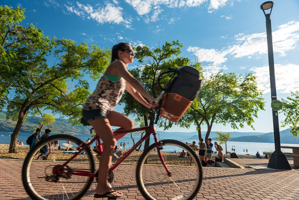 Girl riding a bicycle on the pathway nearby the beach with a bag