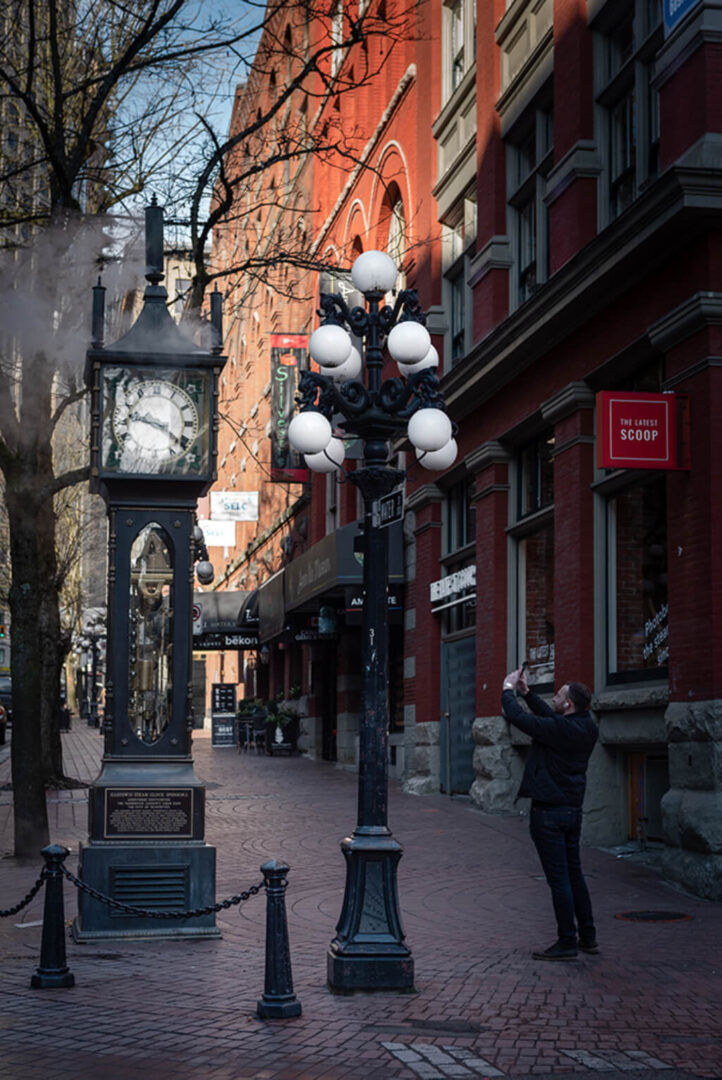 Man clicking photographs of a town Clock on a street