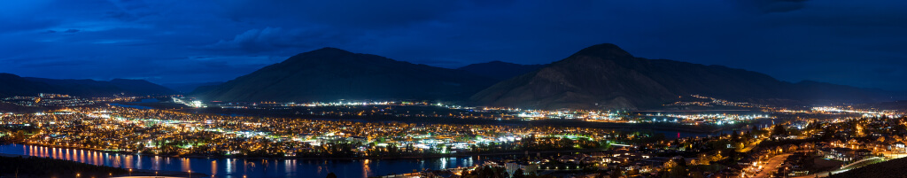 Brightly light city at night with dark blue sky and mountain