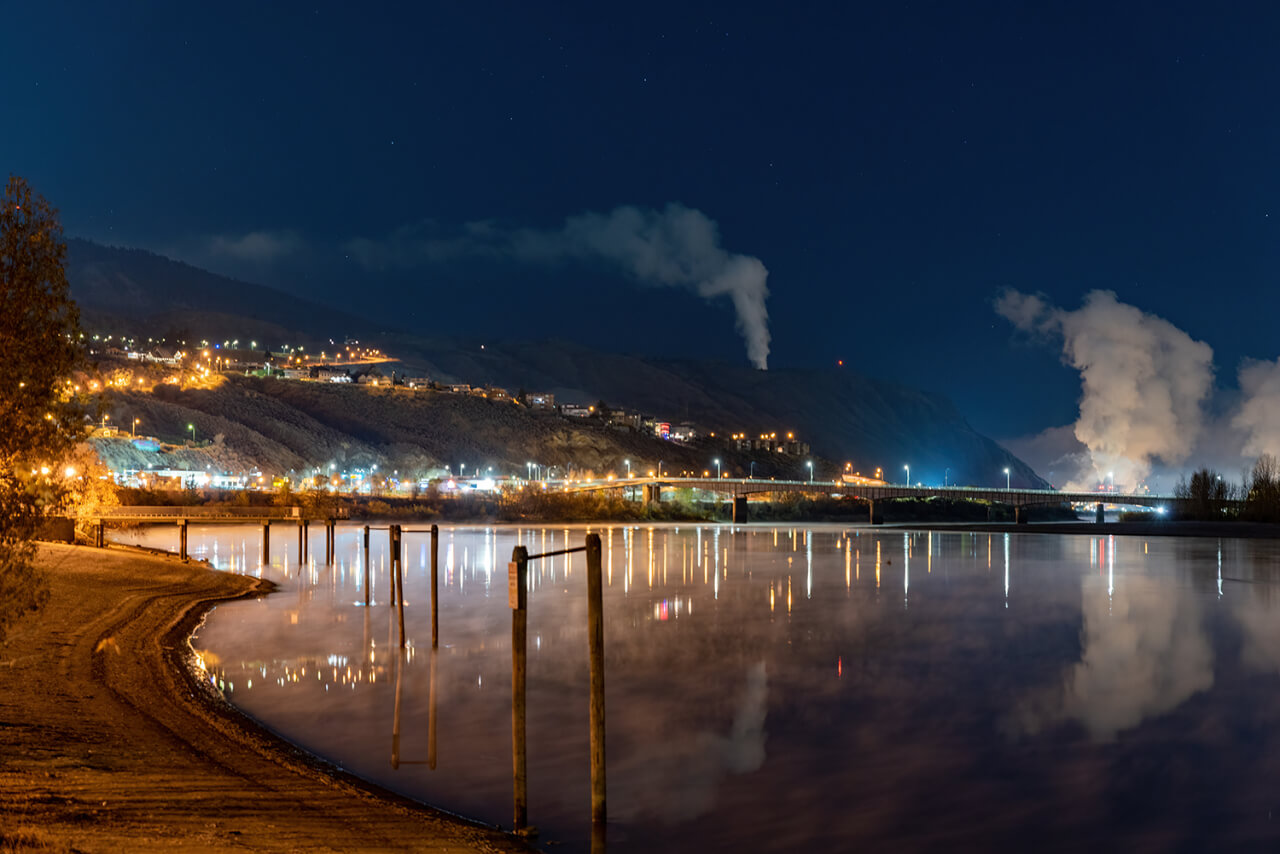 The lakeside view of city at night with smoke and mountains