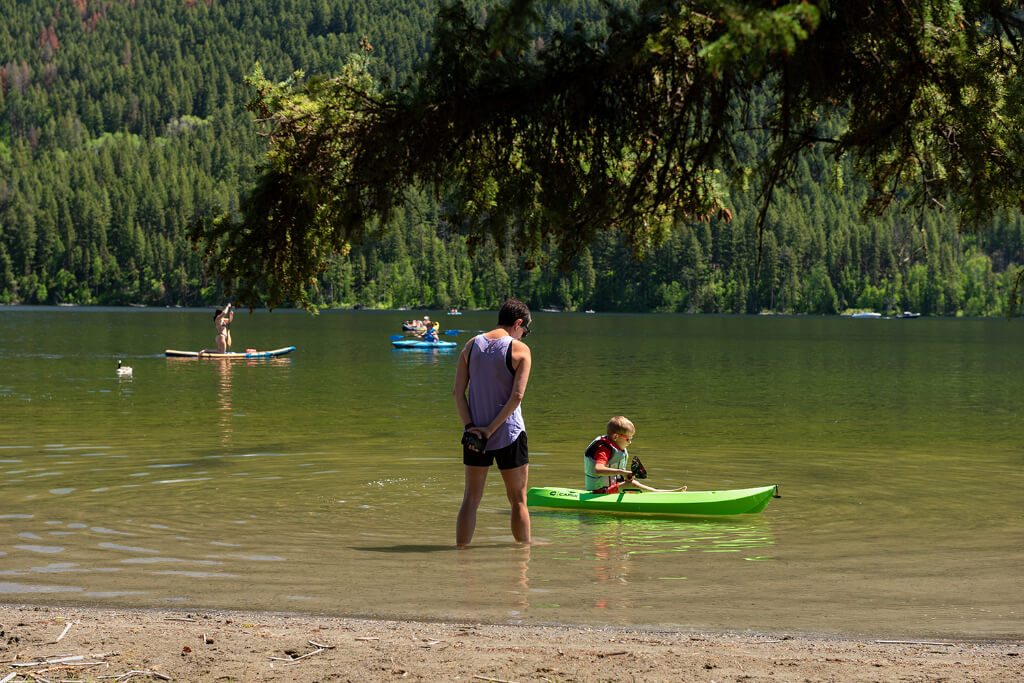 Parent watching child row a kayak in a lake