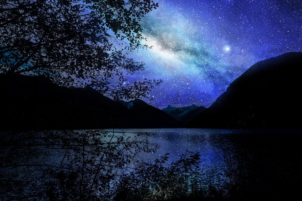 A black sky covered with stars above a river and mountains